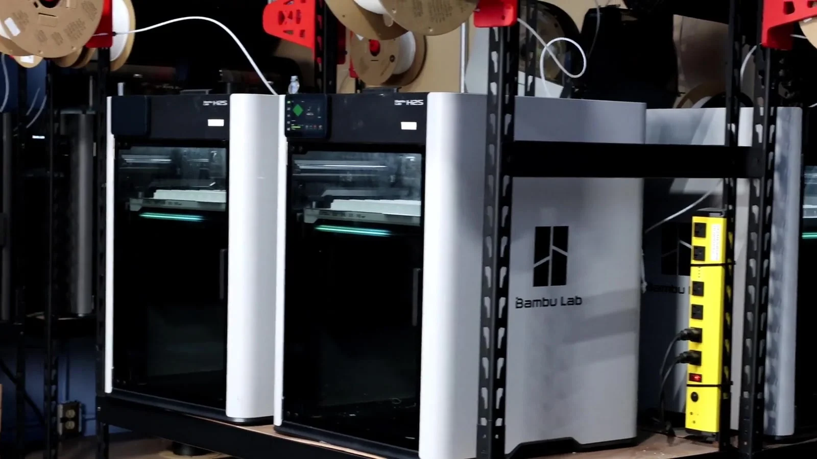 Shelving racked with Bambu Lab 3D printers running, filament spools feeding in from above