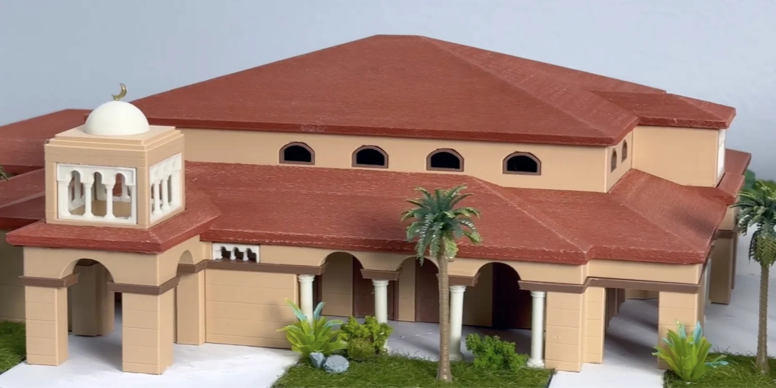 Colored 3D-printed architectural scale model of a mosque community center with terracotta tile roofs, arched colonnades, palm trees, and a domed minaret topped with a gold crescent