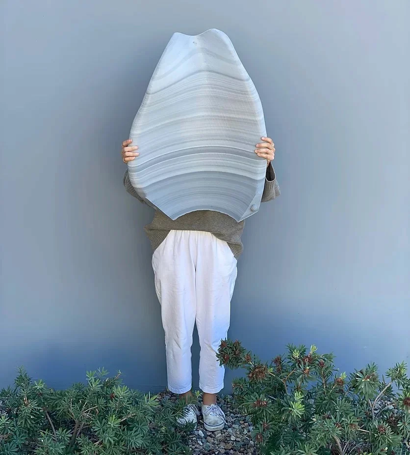 A person holding a large curved 3D-printed panel in front of them, the panel reaching from their waist to above their head