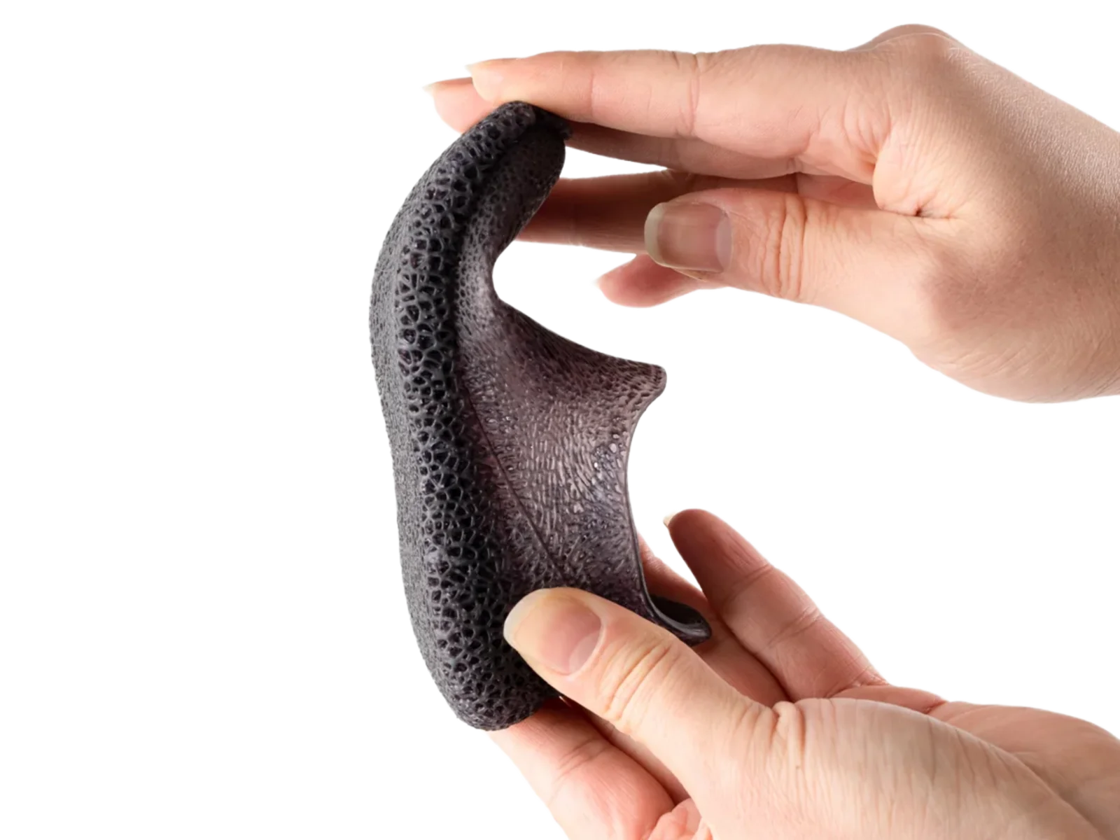 Two hands flexing a dark grey 3D-printed flexible resin part with a porous lattice structure to demonstrate its pliability