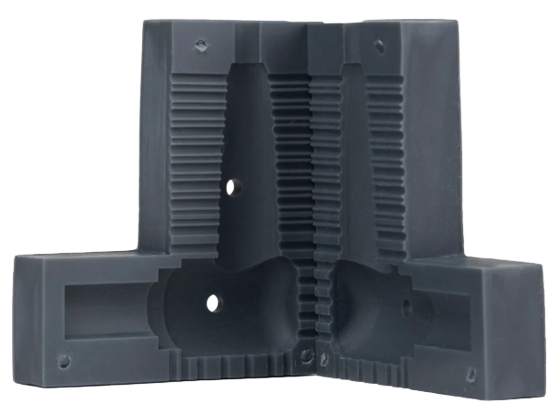 Dark charcoal 3D-printed two-part tooling block in high-temperature resin, its mirrored halves carrying matching ribbed cavities and corner bolt holes
