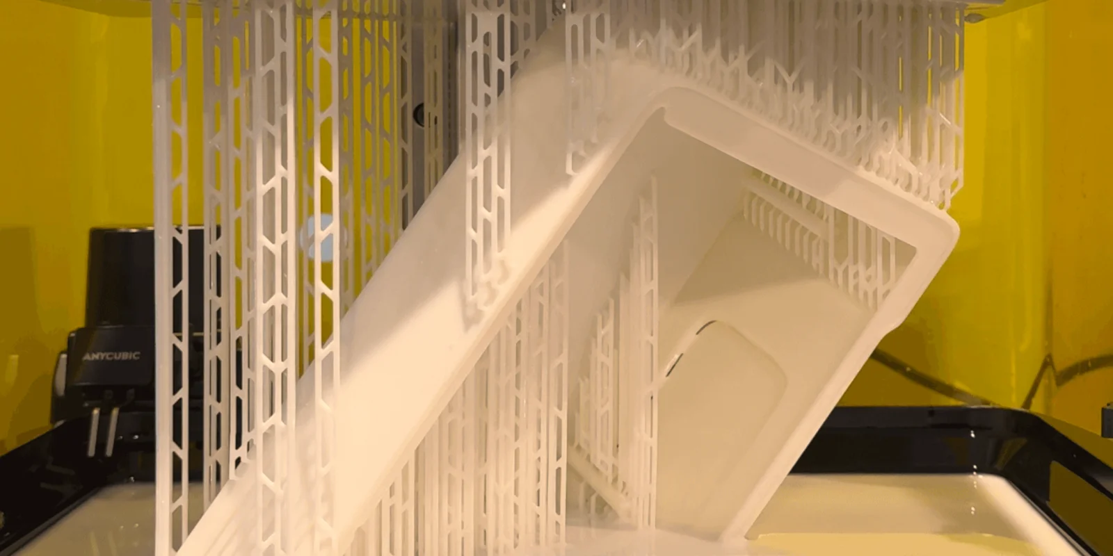 Close-up of a white 3D-printed part suspended on supports inside a stereolithography printer mid-print