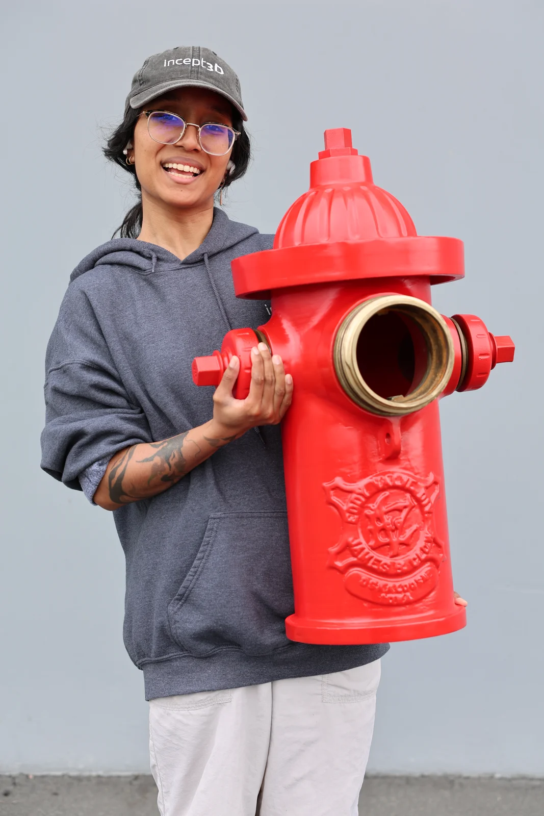 An Incept 3D team member holding a large red painted 3D-printed fire hydrant with brass outlet and cap fittings